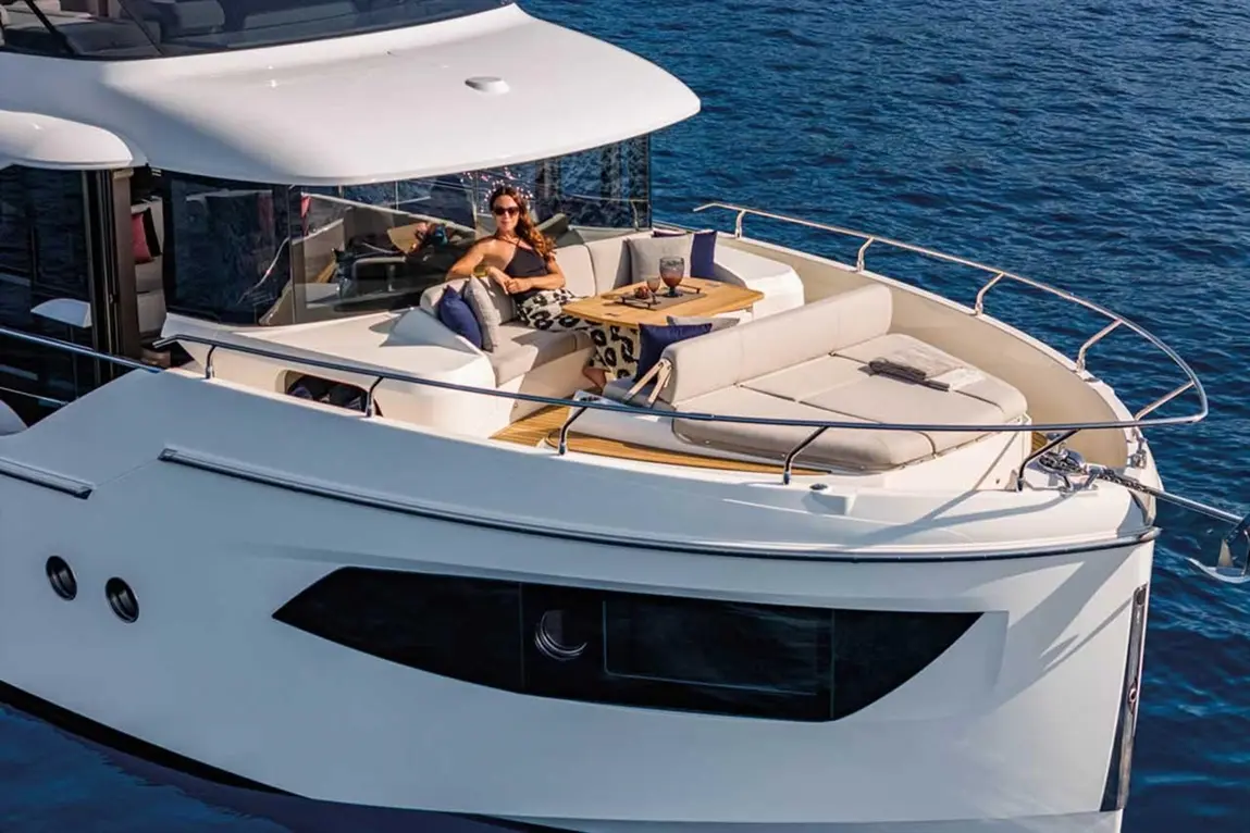 A woman relaxes on a luxury yacht's deck, enjoying a drink and snacks, surrounded by plush seating and blue water.